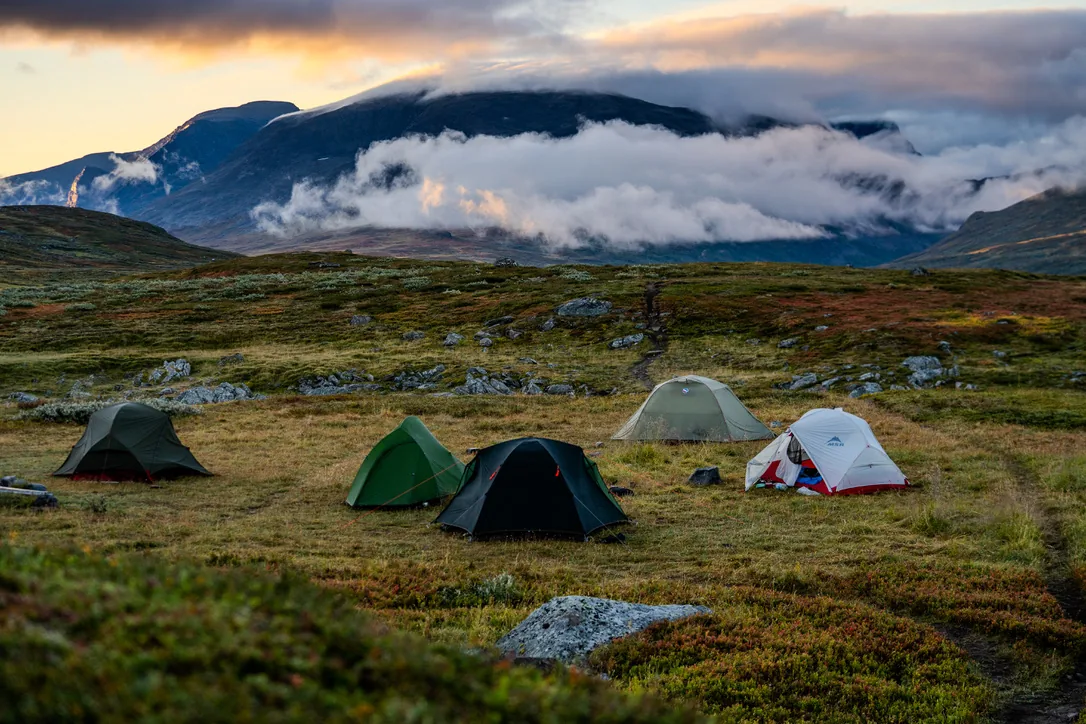 Several tents on autumn tundra at sunset, with cloud-wrapped mountains behind